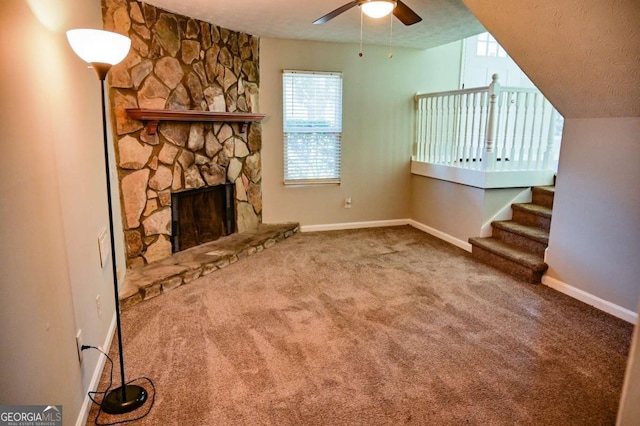 unfurnished living room with ceiling fan, carpet flooring, a stone fireplace, and a textured ceiling