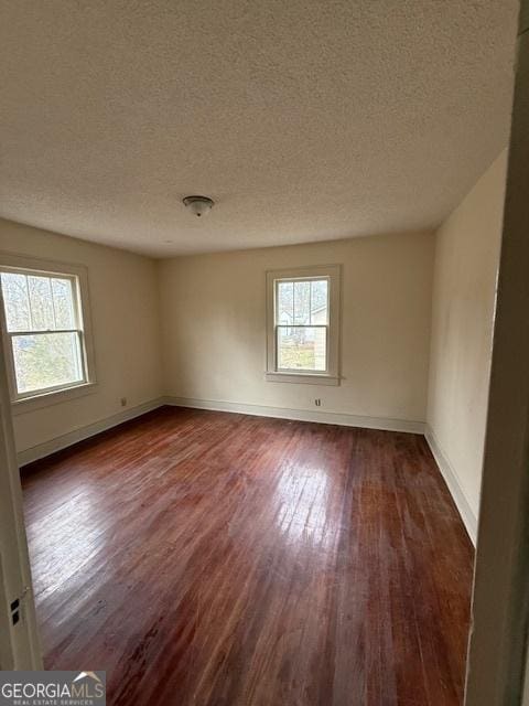 spare room featuring dark hardwood / wood-style floors, a wealth of natural light, and a textured ceiling