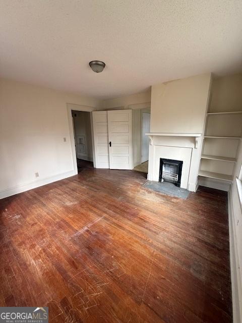 unfurnished living room featuring a textured ceiling and dark hardwood / wood-style flooring