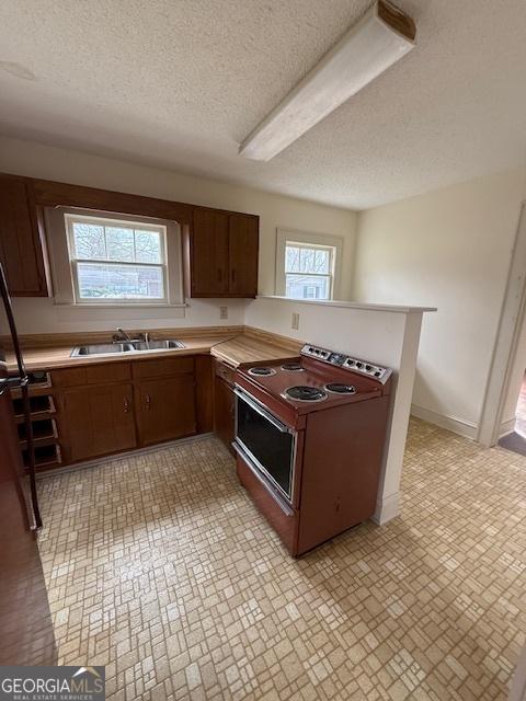 kitchen with sink, kitchen peninsula, a textured ceiling, and range