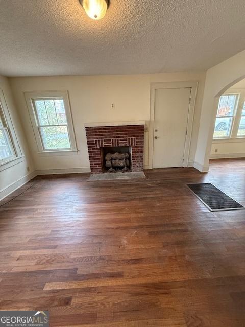 unfurnished living room featuring hardwood / wood-style flooring, a healthy amount of sunlight, a textured ceiling, and a fireplace