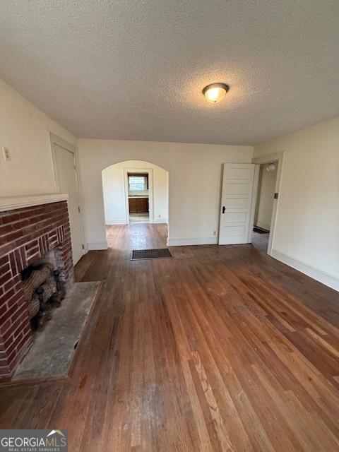 unfurnished living room with a brick fireplace, dark wood-type flooring, and a textured ceiling