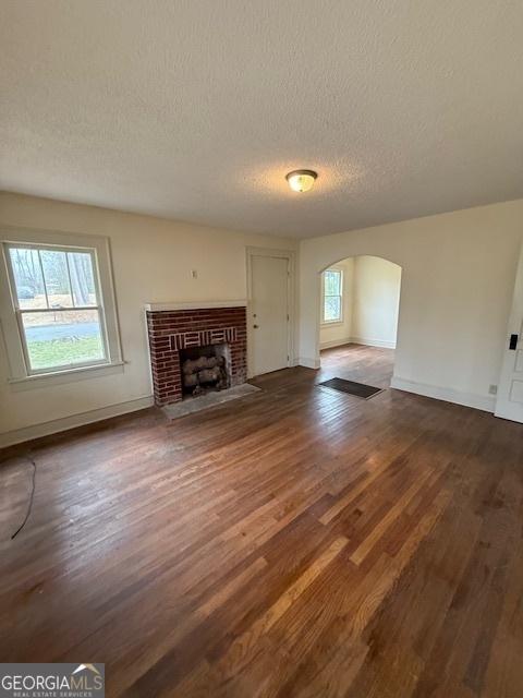 unfurnished living room with a brick fireplace, dark wood-type flooring, and a textured ceiling