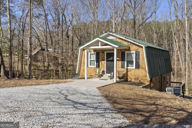 view of front of home featuring entry steps, central AC unit, a gambrel roof, a forest view, and metal roof