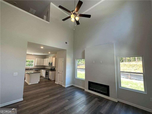 unfurnished living room with dark hardwood / wood-style floors, sink, ceiling fan, and a towering ceiling