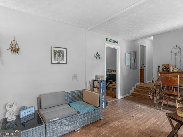 living room featuring wood-type flooring, electric panel, and a textured ceiling