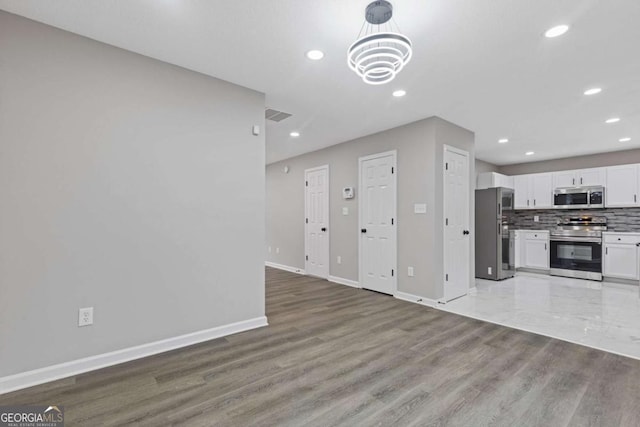 kitchen featuring appliances with stainless steel finishes, wood-type flooring, white cabinets, decorative backsplash, and an inviting chandelier