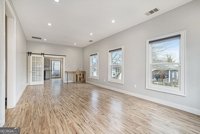 unfurnished living room with a barn door and light hardwood / wood-style flooring