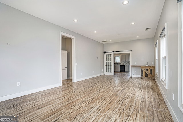 unfurnished living room featuring a barn door, sink, and light hardwood / wood-style flooring