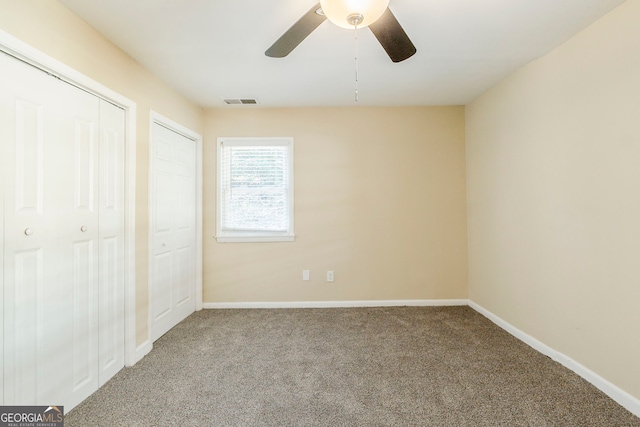 unfurnished bedroom featuring ceiling fan, carpet flooring, and two closets