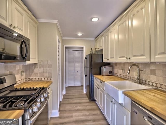 kitchen featuring butcher block counters, sink, ornamental molding, black appliances, and light wood-type flooring