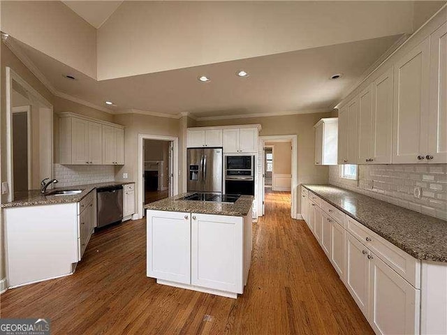 kitchen with appliances with stainless steel finishes, white cabinetry, sink, dark stone countertops, and dark hardwood / wood-style flooring