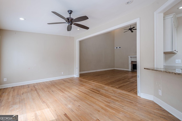 unfurnished living room featuring a fireplace, light wood-type flooring, baseboards, and ceiling fan