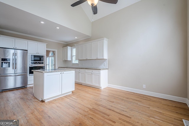 kitchen featuring crown molding, ceiling fan, a center island, appliances with stainless steel finishes, and decorative backsplash