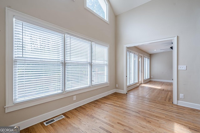 empty room featuring baseboards, visible vents, ceiling fan, high vaulted ceiling, and wood finished floors