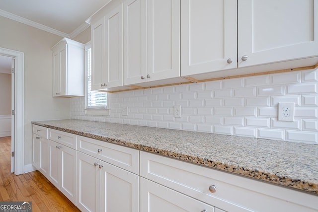 kitchen with light wood-style floors, crown molding, white cabinetry, light stone countertops, and backsplash