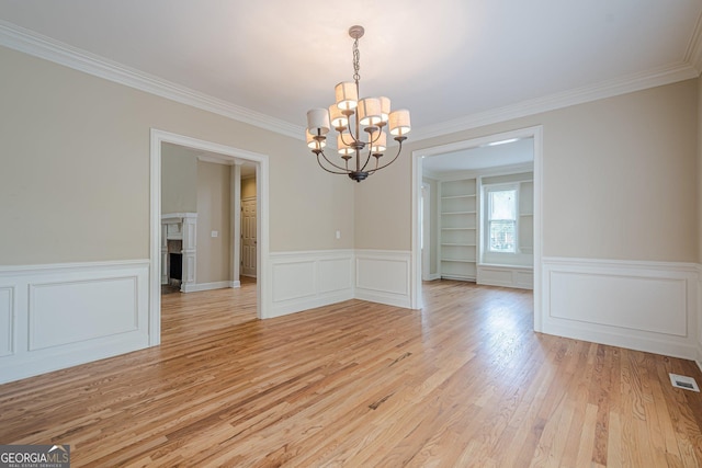unfurnished dining area featuring a notable chandelier, a decorative wall, ornamental molding, light wood-type flooring, and wainscoting