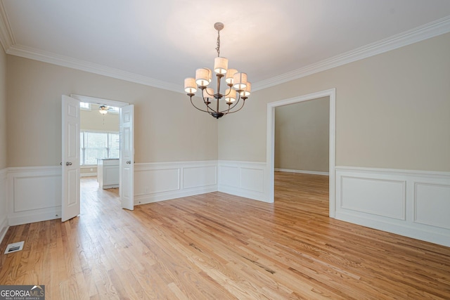 unfurnished dining area with crown molding, an inviting chandelier, light wood-style flooring, visible vents, and wainscoting