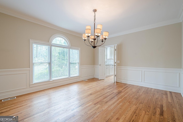 unfurnished room featuring a chandelier, crown molding, a wainscoted wall, light wood-style floors, and visible vents