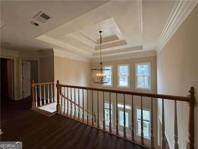 hall with hardwood / wood-style floors, a notable chandelier, ornamental molding, and a raised ceiling