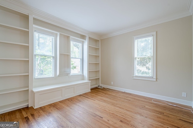 empty room with baseboards, built in shelves, light wood-type flooring, and crown molding