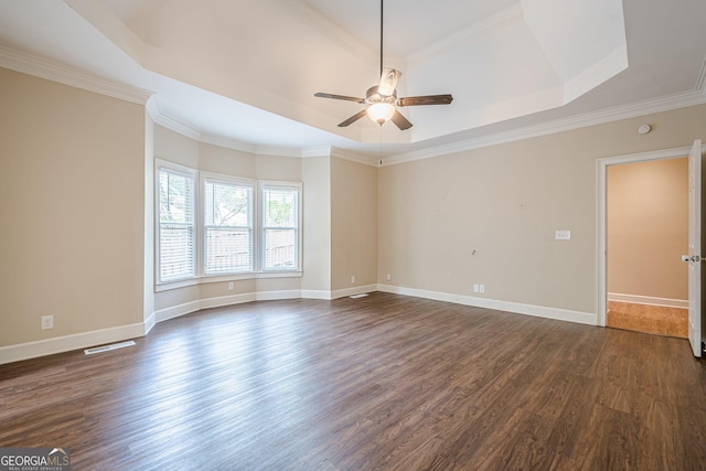 spare room with a tray ceiling, ornamental molding, a ceiling fan, baseboards, and dark wood-style floors