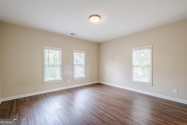 empty room with dark wood-type flooring, visible vents, a wealth of natural light, and baseboards
