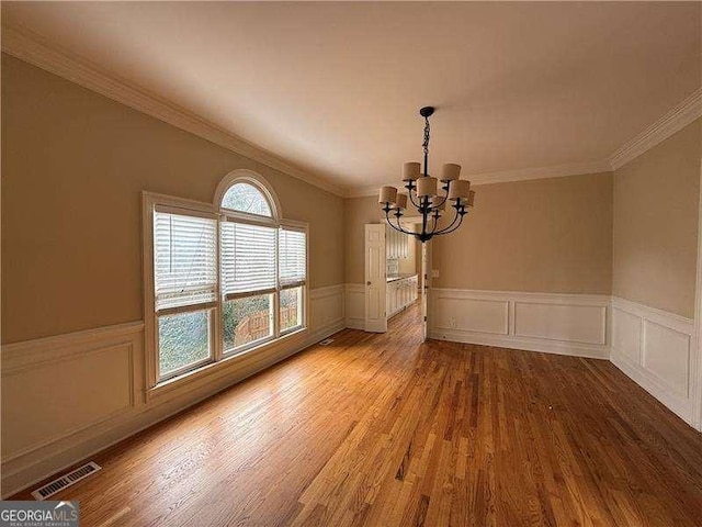 unfurnished dining area featuring wood-type flooring, a notable chandelier, and crown molding