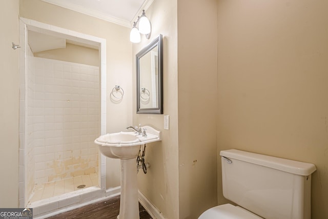 bathroom featuring baseboards, a stall shower, crown molding, toilet, and a sink