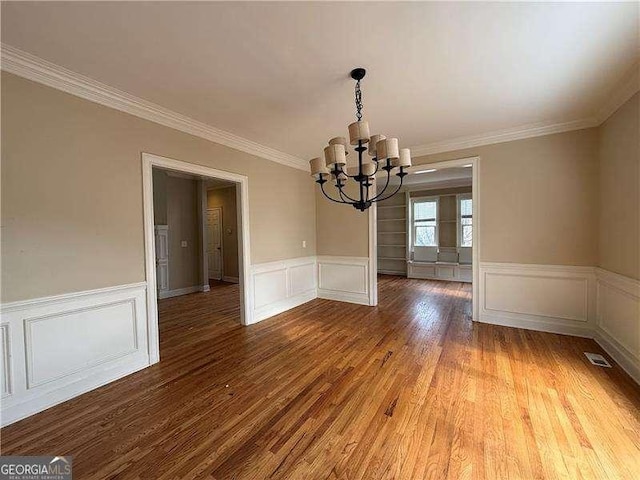 unfurnished dining area featuring crown molding, hardwood / wood-style floors, and a notable chandelier