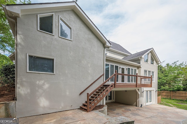 rear view of property featuring stucco siding, stairway, a patio area, a deck, and fence