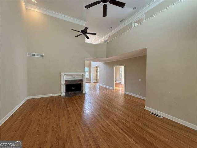 unfurnished living room featuring ceiling fan, hardwood / wood-style floors, a towering ceiling, a high end fireplace, and ornamental molding