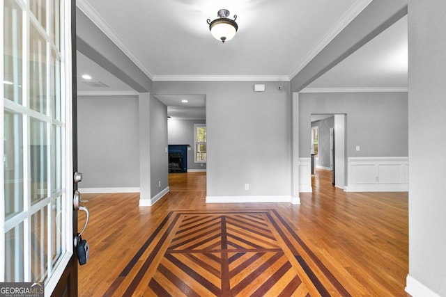 foyer entrance featuring a wainscoted wall, a fireplace, wood finished floors, and crown molding