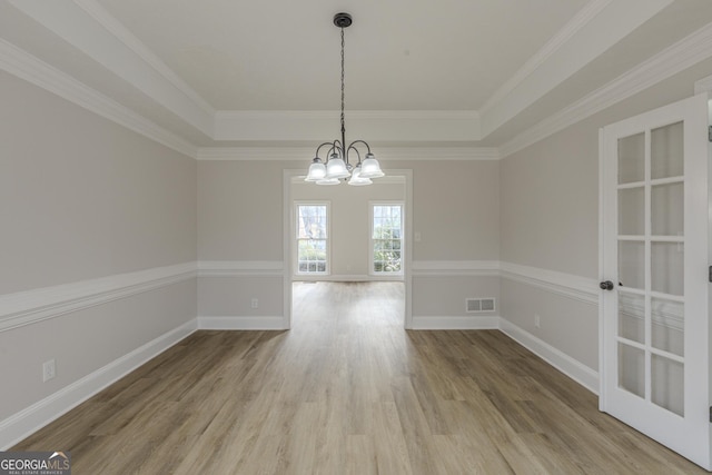 unfurnished dining area featuring crown molding, hardwood / wood-style floors, an inviting chandelier, and a tray ceiling