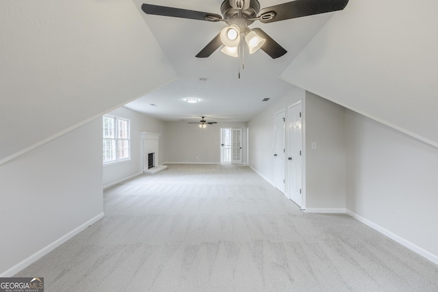 bonus room with a brick fireplace, light colored carpet, and ceiling fan