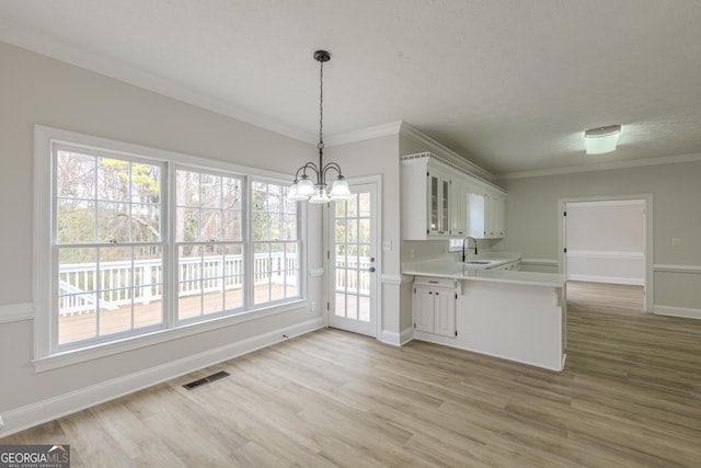 kitchen with decorative light fixtures, white cabinetry, sink, light hardwood / wood-style floors, and kitchen peninsula