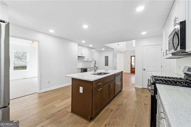 kitchen with appliances with stainless steel finishes, sink, white cabinets, a kitchen island with sink, and light hardwood / wood-style floors