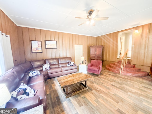 living room with ceiling fan, wood-type flooring, and wooden walls