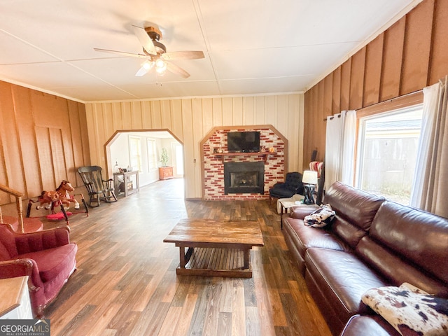 living room with dark wood-type flooring, ceiling fan, a brick fireplace, and wood walls