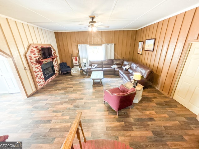 living room featuring dark wood-type flooring, ceiling fan, a fireplace, and wooden walls