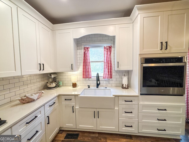 kitchen with white cabinetry, sink, backsplash, dark hardwood / wood-style flooring, and stainless steel oven