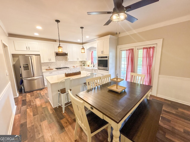 dining space with ornamental molding, sink, dark wood-type flooring, and ceiling fan