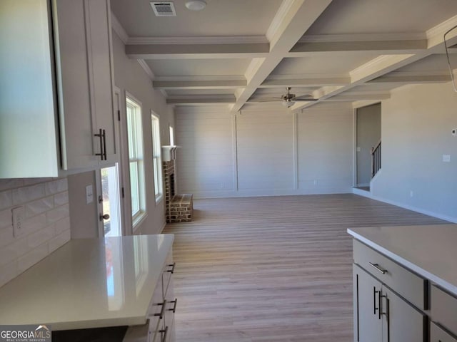 interior space with ceiling fan, coffered ceiling, a fireplace, beamed ceiling, and light wood-type flooring