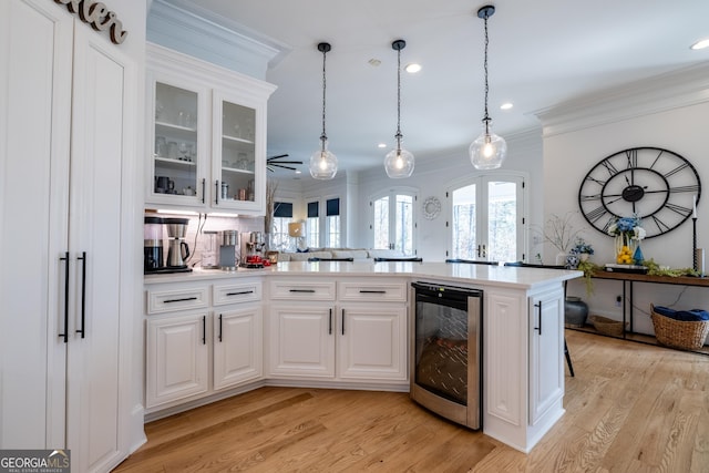 kitchen with crown molding, light hardwood / wood-style flooring, white cabinetry, hanging light fixtures, and beverage cooler