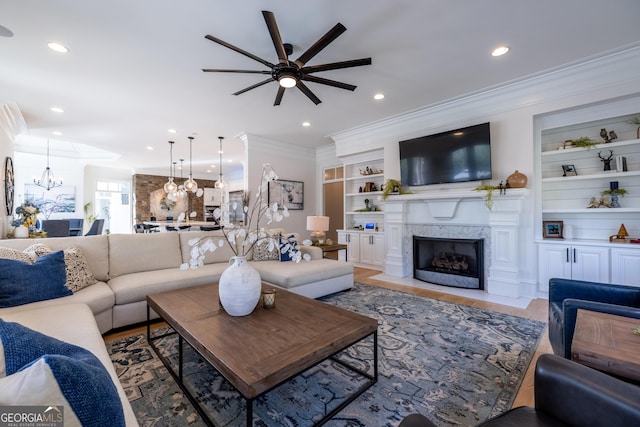 living room featuring built in shelves, crown molding, an inviting chandelier, wood-type flooring, and a high end fireplace