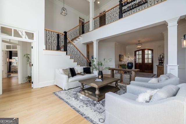 living room featuring a high ceiling, wood-type flooring, ornamental molding, french doors, and ornate columns