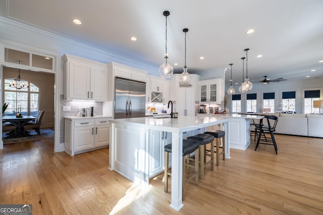 kitchen featuring a large island with sink, stainless steel built in fridge, a breakfast bar area, and white cabinets