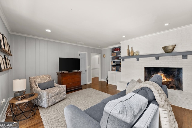 living room with ornamental molding, a brick fireplace, dark hardwood / wood-style floors, and built in shelves