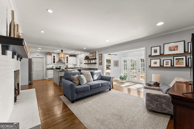 living room with sink, crown molding, a fireplace, wood-type flooring, and french doors