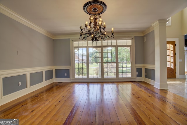 unfurnished room featuring decorative columns, crown molding, wood-type flooring, and an inviting chandelier